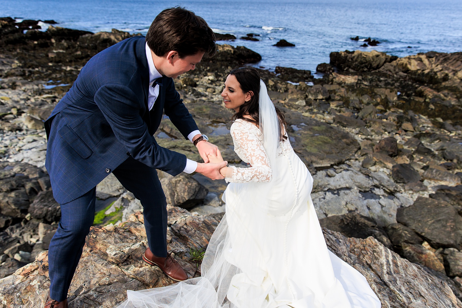The groom helps the bride up the rocks of Marginal Way
