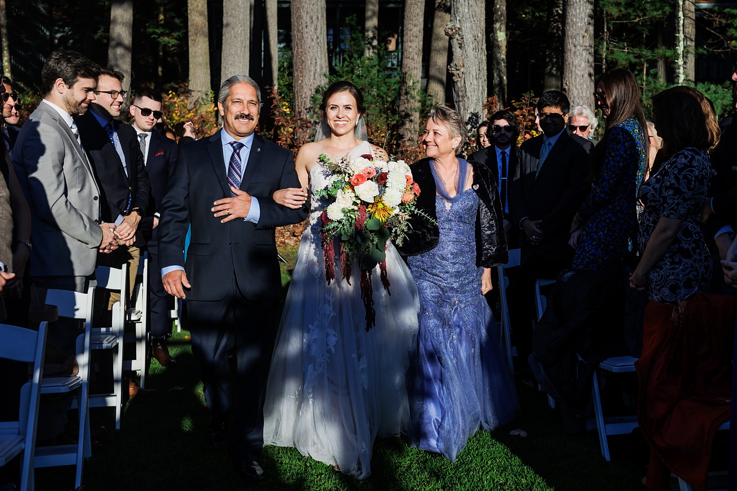 The bride and her parents come down the aisle on the sunny fall day