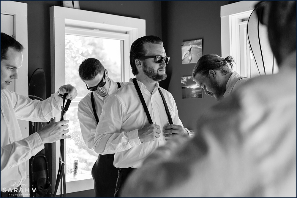 The groomsmen help the groom get into his wedding day attire in Maine