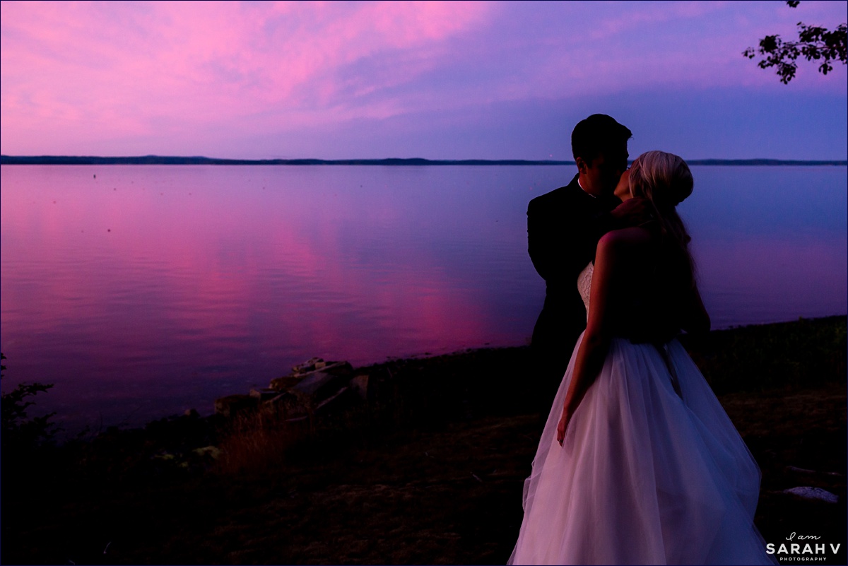 The bride and groom kiss in front of the sunset while their reception is in full swing at the Pot & Kettle Club