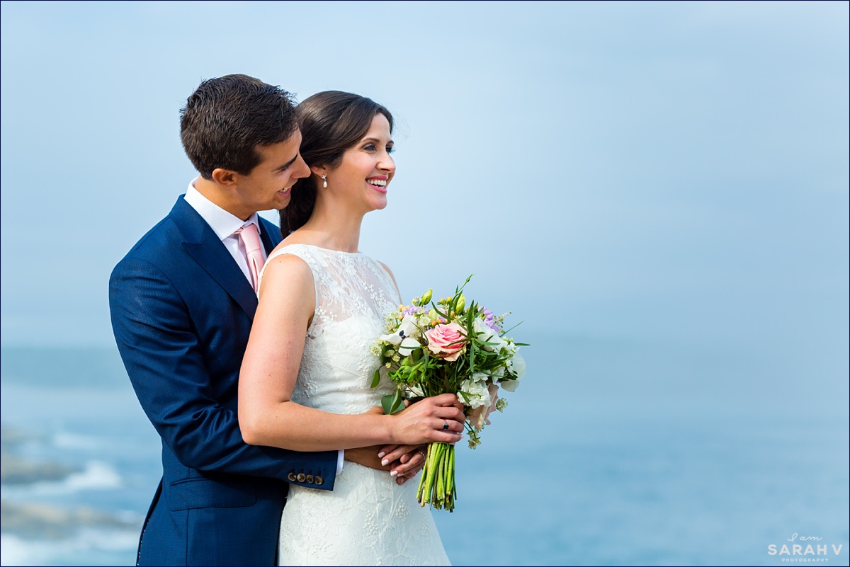 The bride and groom laugh together while standing on the cliffs in Acadia after their wedding ceremony