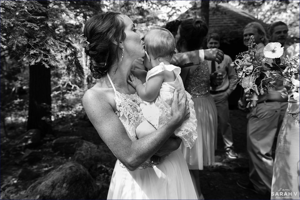 The bride kisses her daughter after the ceremony is complete with her wedding party celebrating behind her in New Hampshire