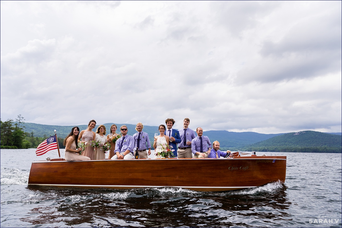 Squam Lake in New Hampshire wedding the newlyweds and the wedding party all pose for a photo together while taosting with champagne on a Cris Craft boat before the rain starts