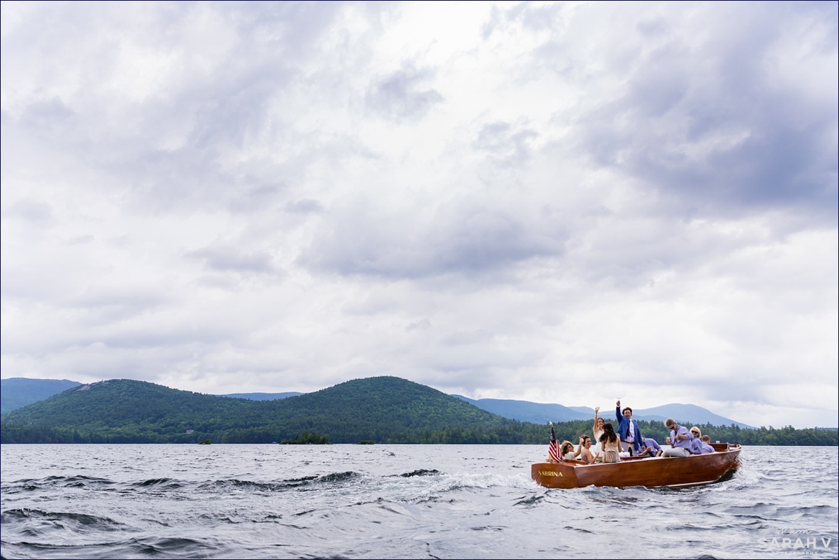 Everyone in the wedding party waves from the Cris Craft boat with the White Mountains NH in the background