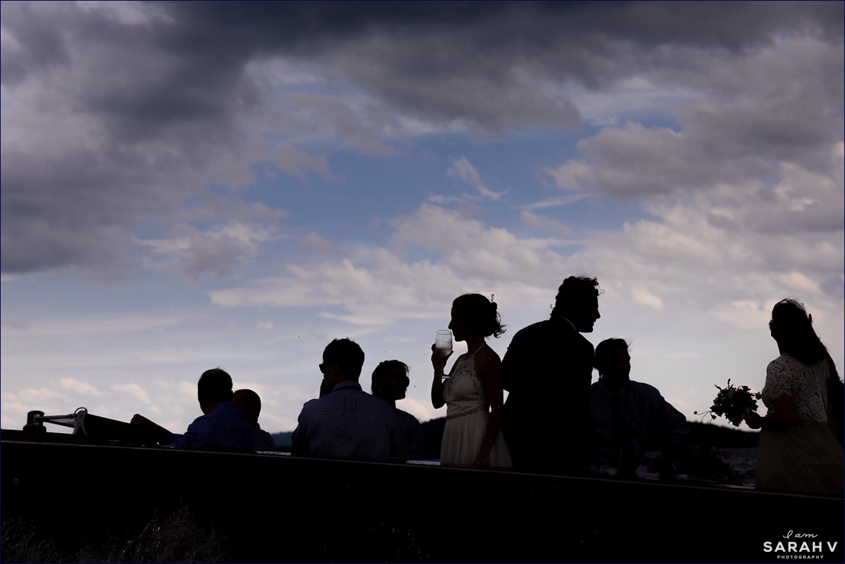 The wedding party and couple are silhouetted against the stormy summer sky on their wedding day while aboard a boat in the White Mountains