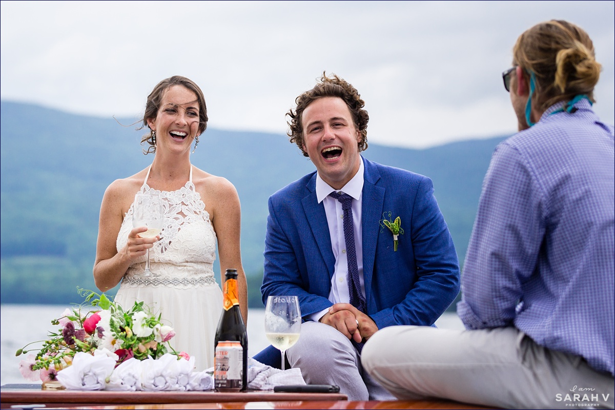The newlyweds share a laugh on the boat with the wedding party - the White Mountains decorate the background at their camp wedding in NH