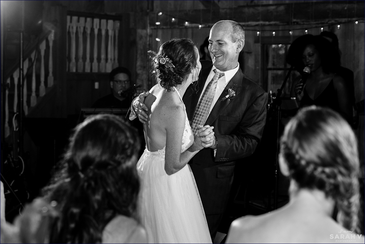 The father of the bride and the bride dance together at the barn reception at the camp wedding