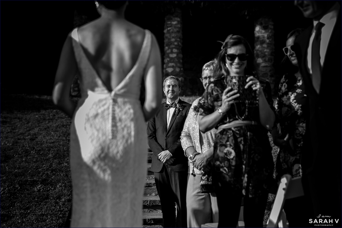 The groom watches as the bride walks down the aisle toward him at the outdoor wedding ceremony