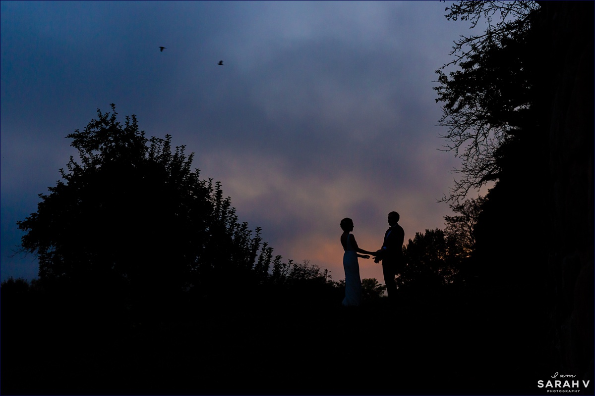 The couple is silhouetted against the sunset sky during a break at their wedding reception in Ipswich MA