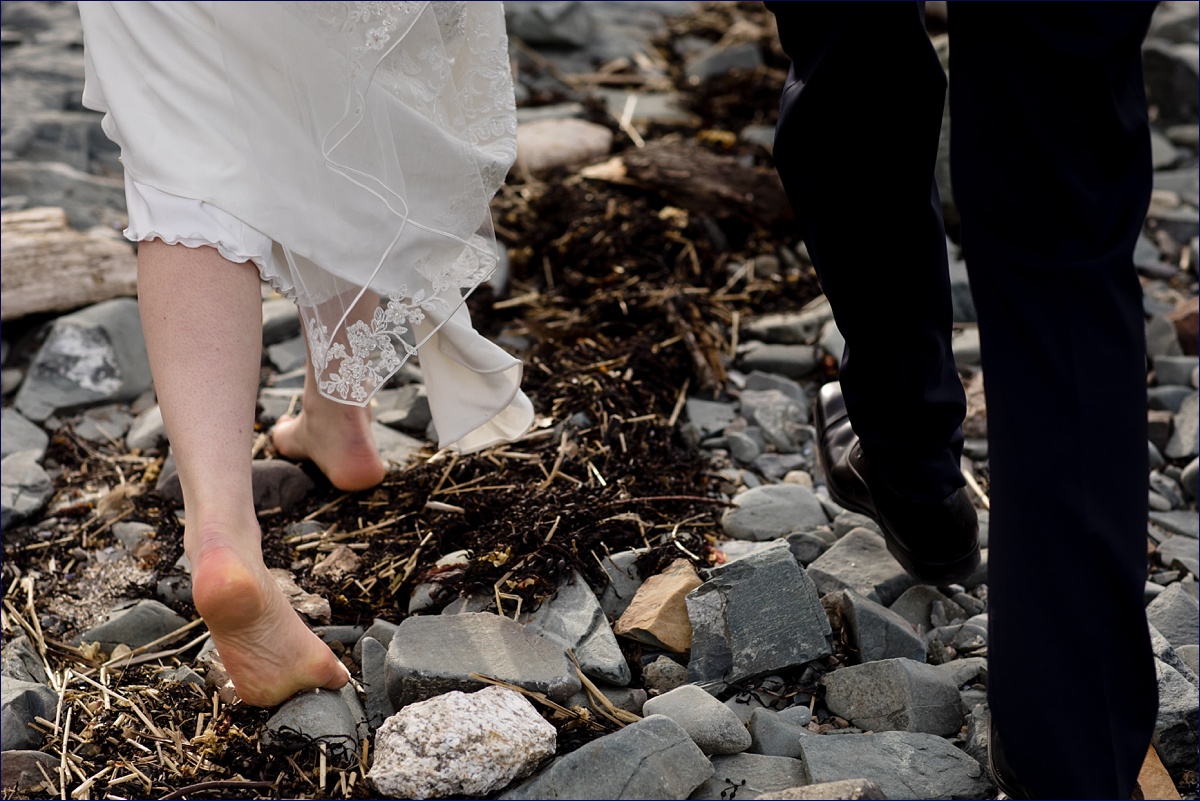 The bride and groom walk along the rocky coastline of Maine for photos