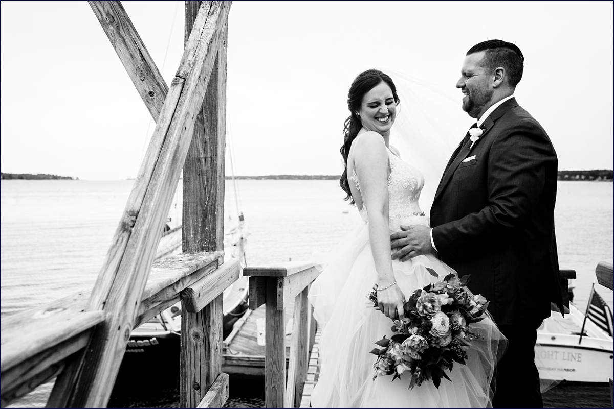 The bride and groom have a laugh with one another on the dock along the ocean