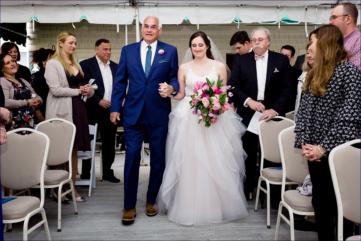 The bride walks down the aisle with her father under the tent
