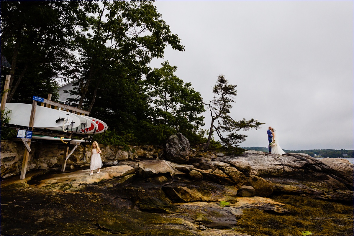Linekin Bay Resort Wedding Photographer in Boothbay Maine the newlyweds hold each other close on the rocks while the flower girl plays in the foreground