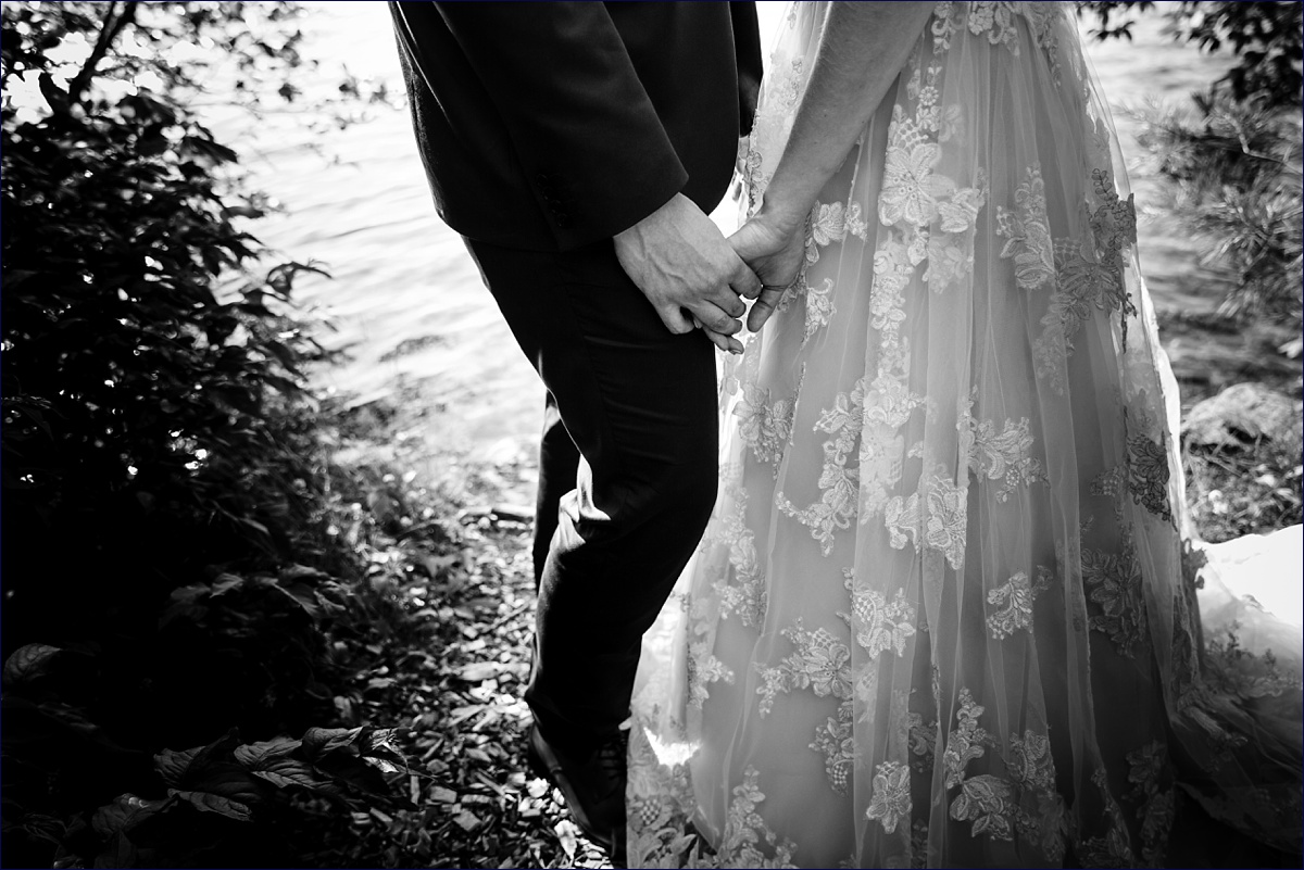 The bride and groom hold hands close to the lake on their wedding day
