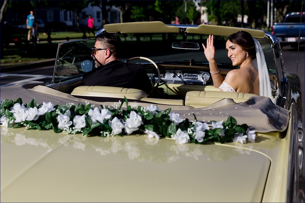 The bride and groom wave as they head to the reception in a vintage car after their ceremony