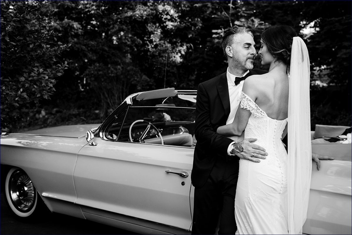 The bride and groom get in close to one another next to their vintage car in Boston