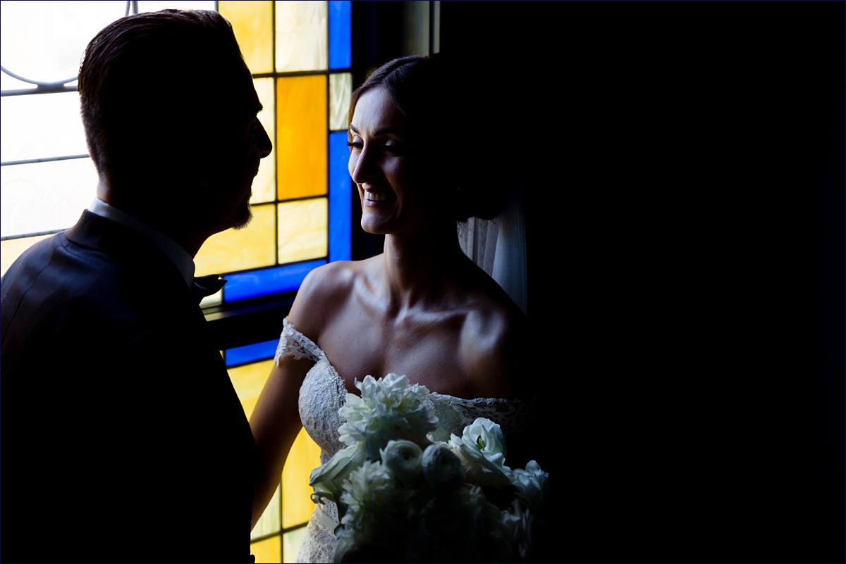 The bride and groom get close in front of the church's stained glass windows on their wedding day