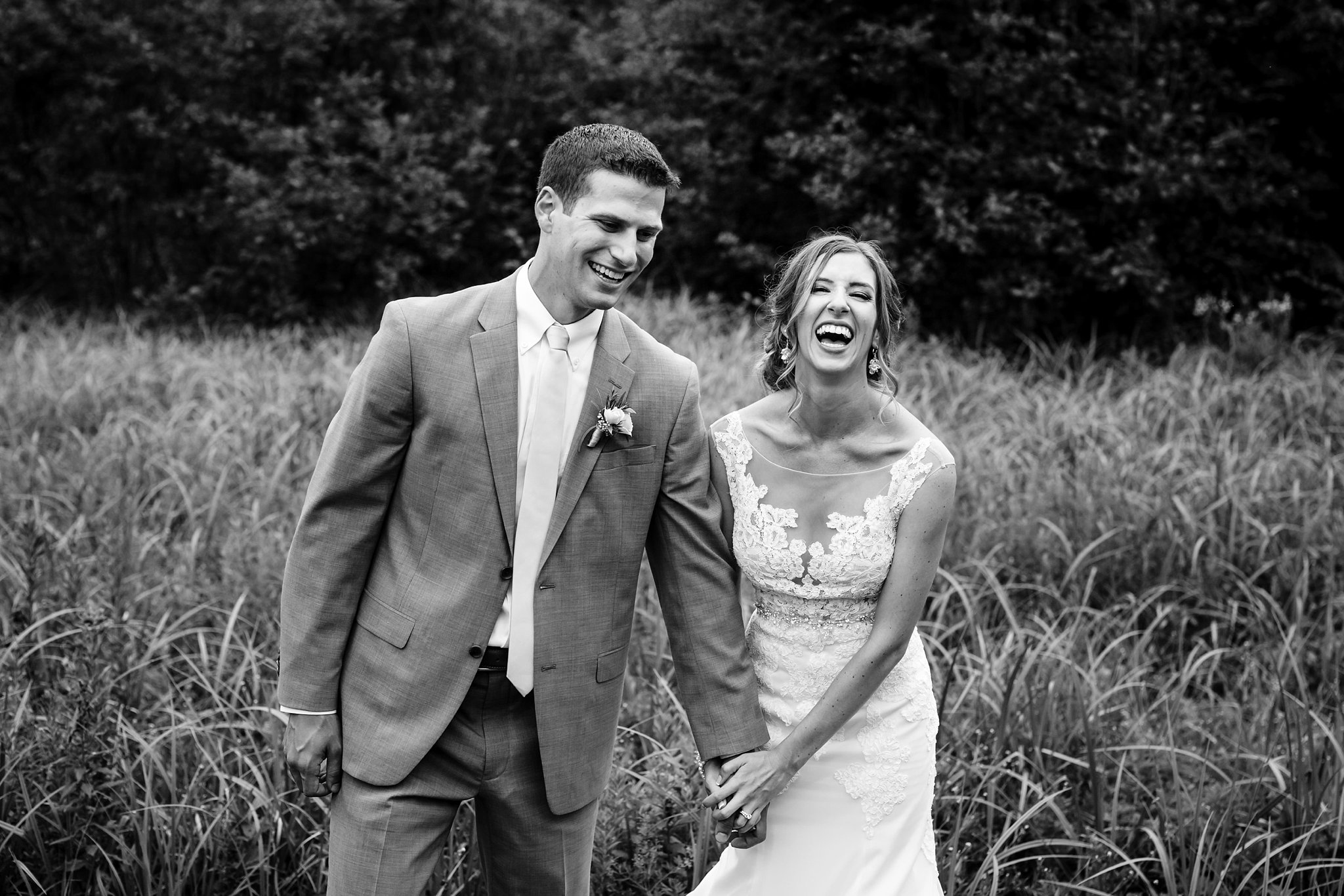 The newlyweds share a laugh before the wedding reception in the tall grass at their outdoor celebration