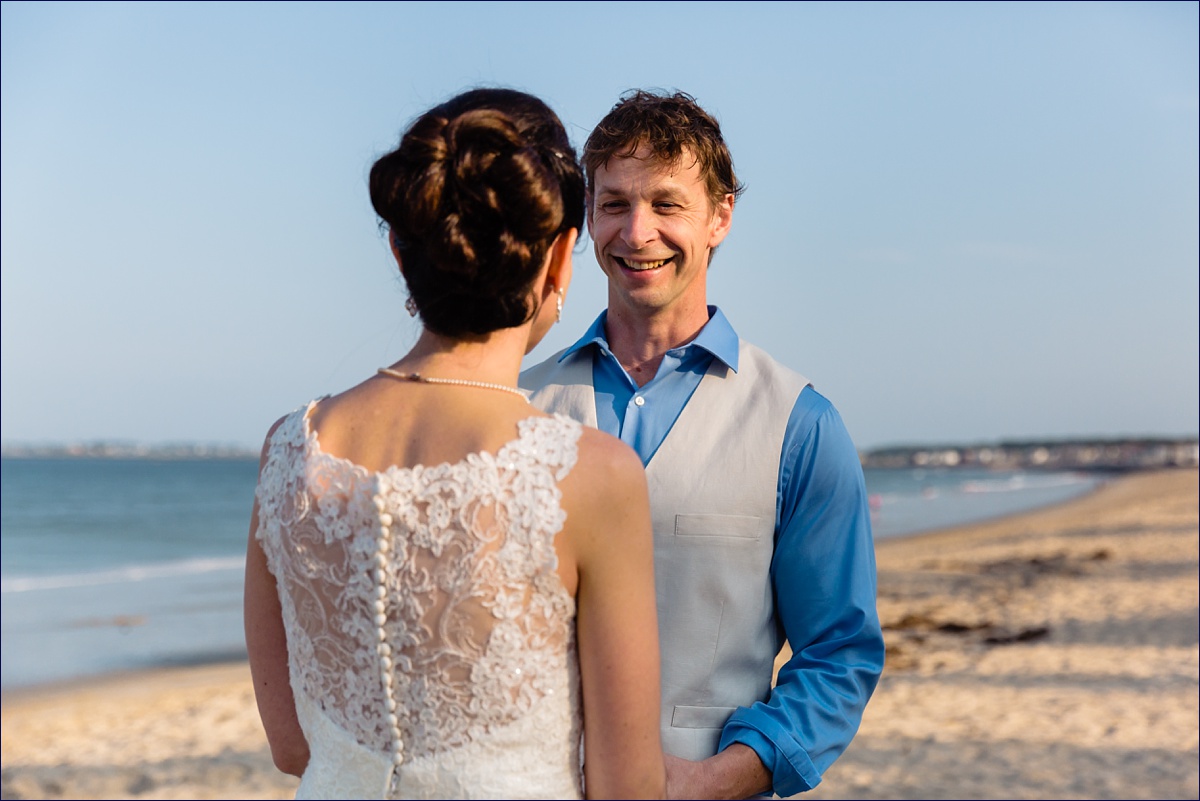 The groom looks at the bride as they say their vows on their intimate Maine beach ceremony