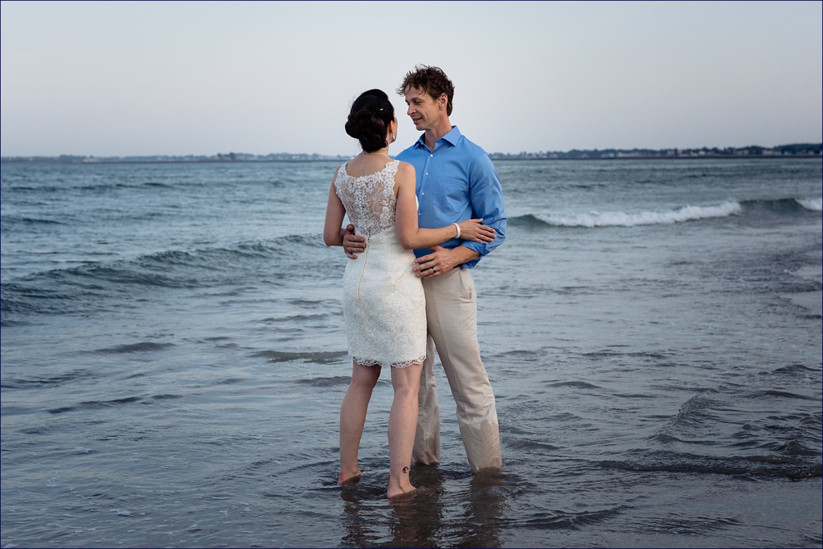 The bride and groom hold each other in the ocean waves before a summer storm settles in