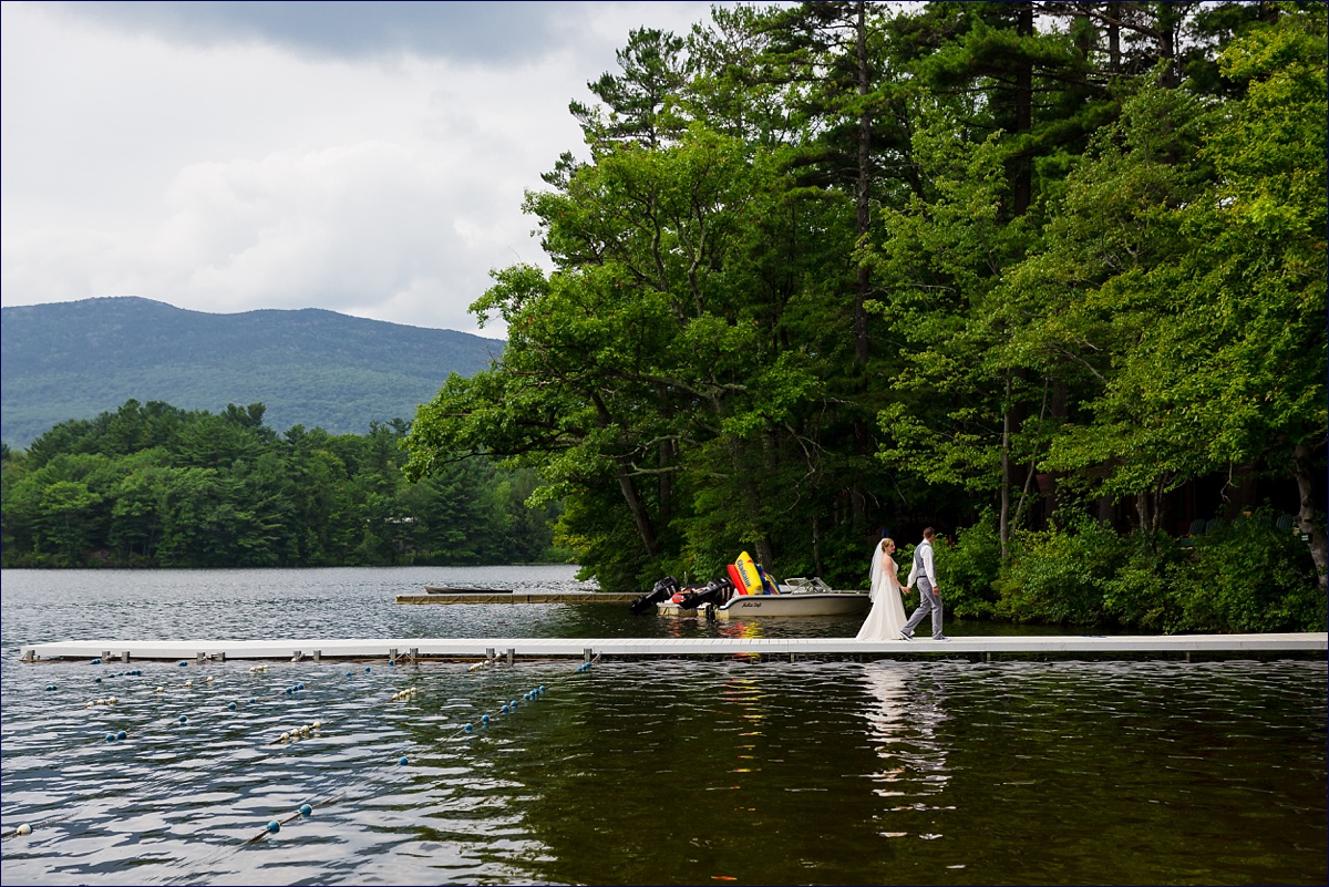 The couple walks on the docks while the mountains serve as a backdrop to their NH wedding day