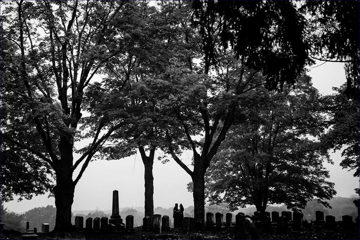 New Hampshire elopement with the bride and groom being silhouetted with the gravestones and the tall fall trees by them