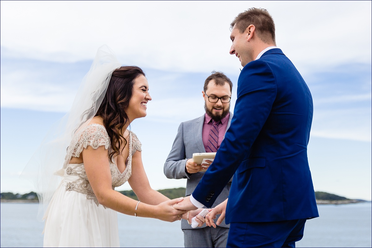The couple laughs during their wedding ceremony on the cliffs at the Portland Headlight in Maine