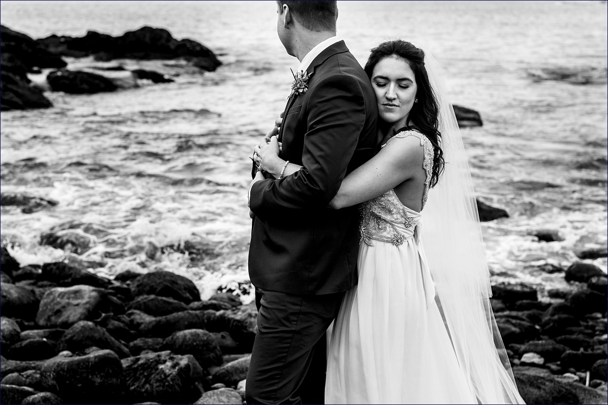 She hugs him tight as he watches the ocean roll over the rocks on their Maine elopement