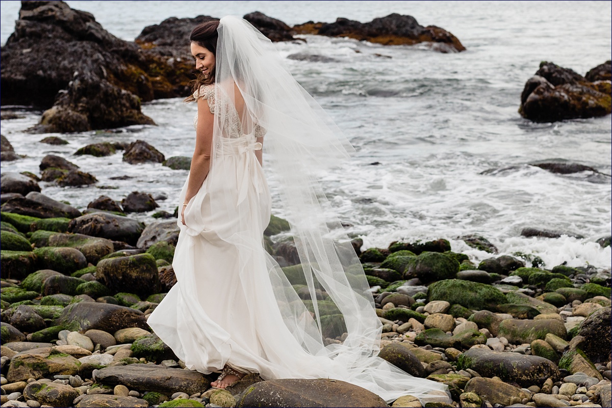 The bride dances in her dress on the algae covered rocks by the ocean in Maine