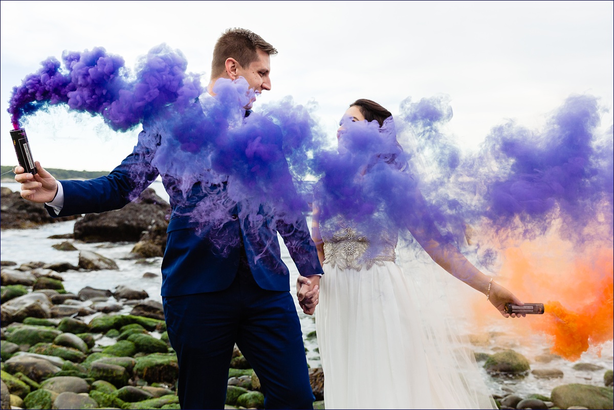 The newlyweds play with colorful smoke bombs at their elopement on the rocky shore of Maine