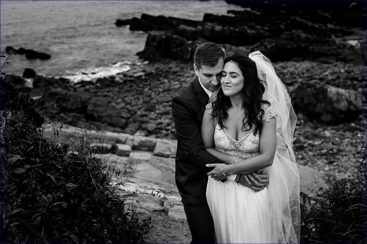 Newlyweds hold each other close near the rocky cliffs over the ocean at their Portland Maine Headlight elopement