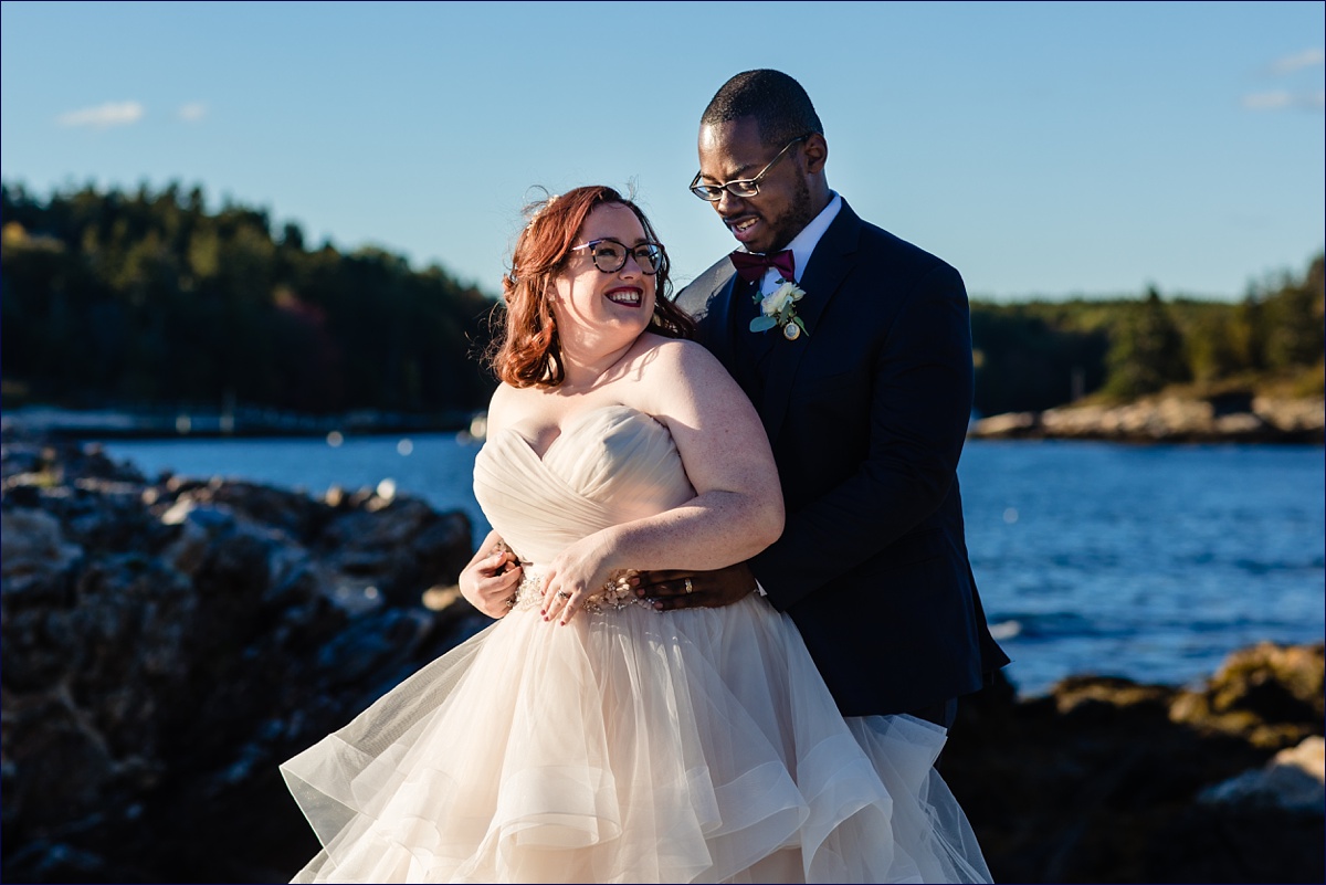 The bride and groom share a laugh on the rocks on their wedding day