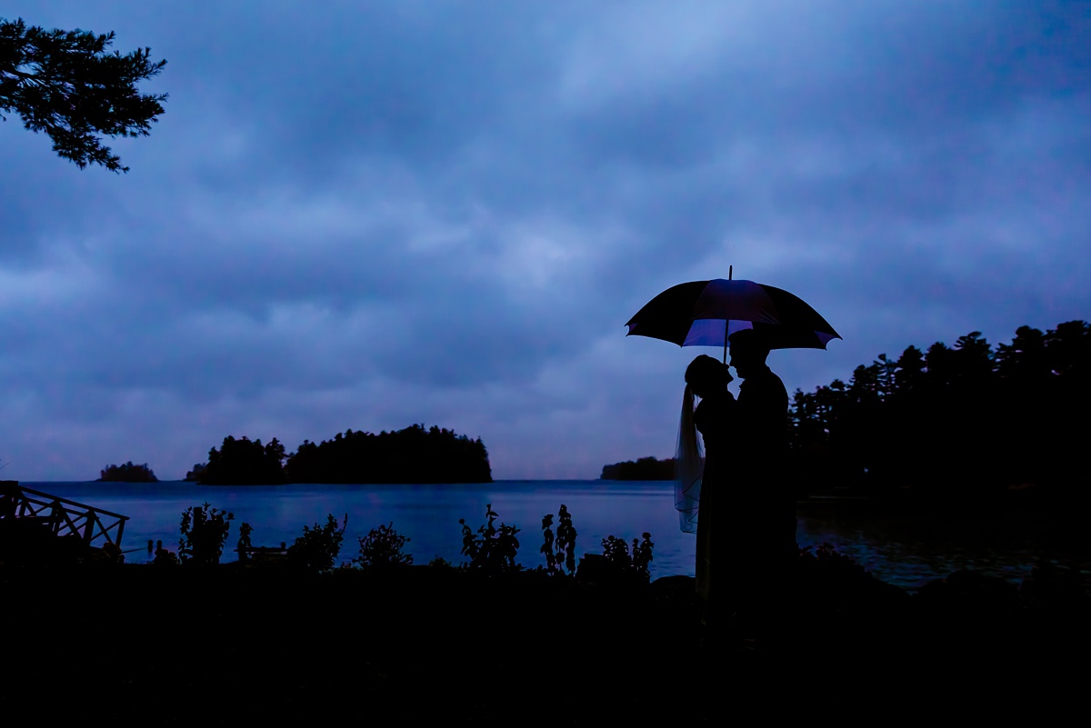The bride and groom are silhouetted against the stormy sky after their ceremony at Migis Lodge in Maine