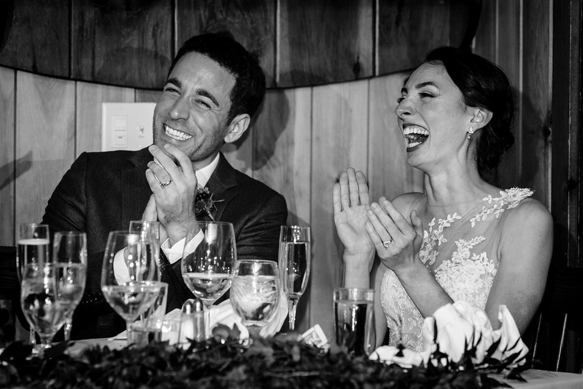 The bride and groom laugh at a toasts during their Migis Lodge Wedding reception