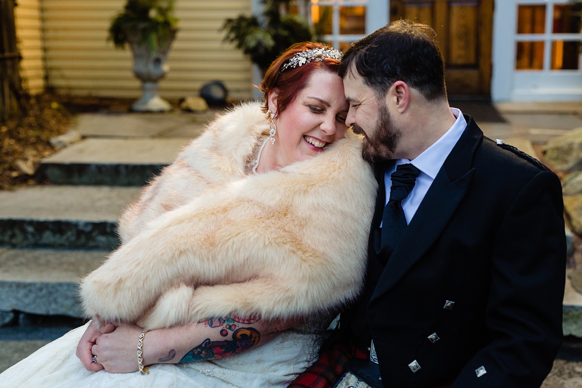 The bride and groom laugh together while keeping warm on their chilly December wedding