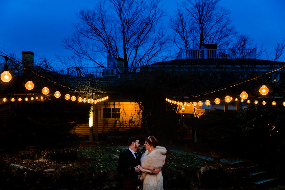 The bride and groom stay close to one another under the twinkle lights on their December wedding day in NH