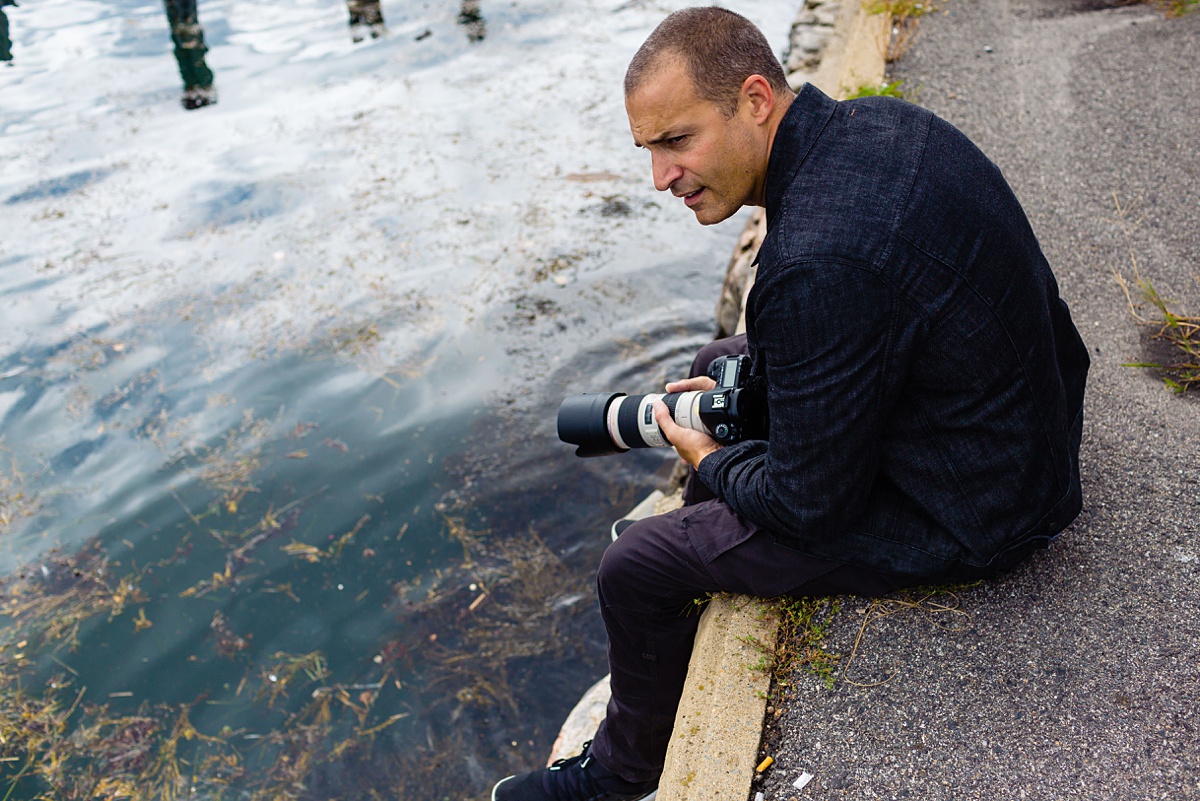 Nigel Barker sits with his feet dangling over the Atlantic ocean in downtown Portland Maine for a photo walking tour