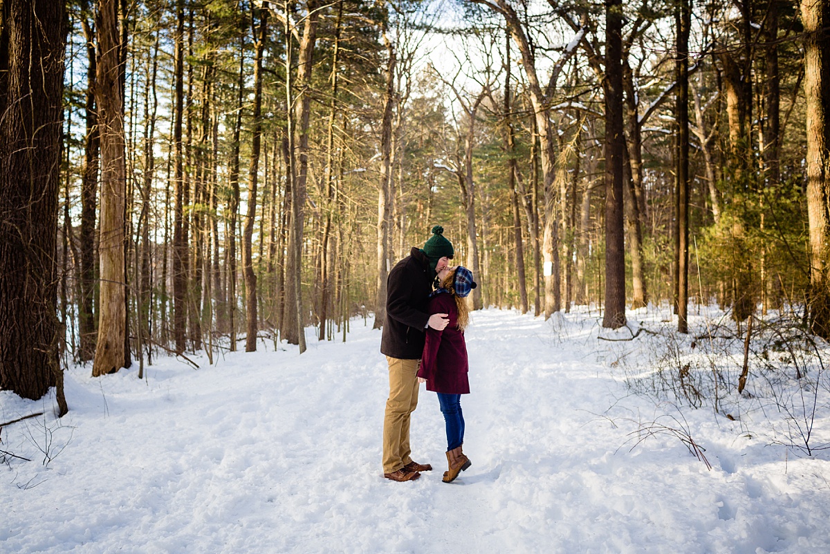 The newly engaged couple kiss in the winter at snowy Fells Reservation MA