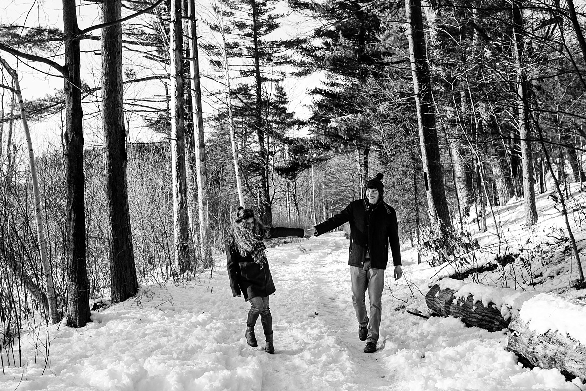 The couple walks through the woods on a snow covered path for their engagement session