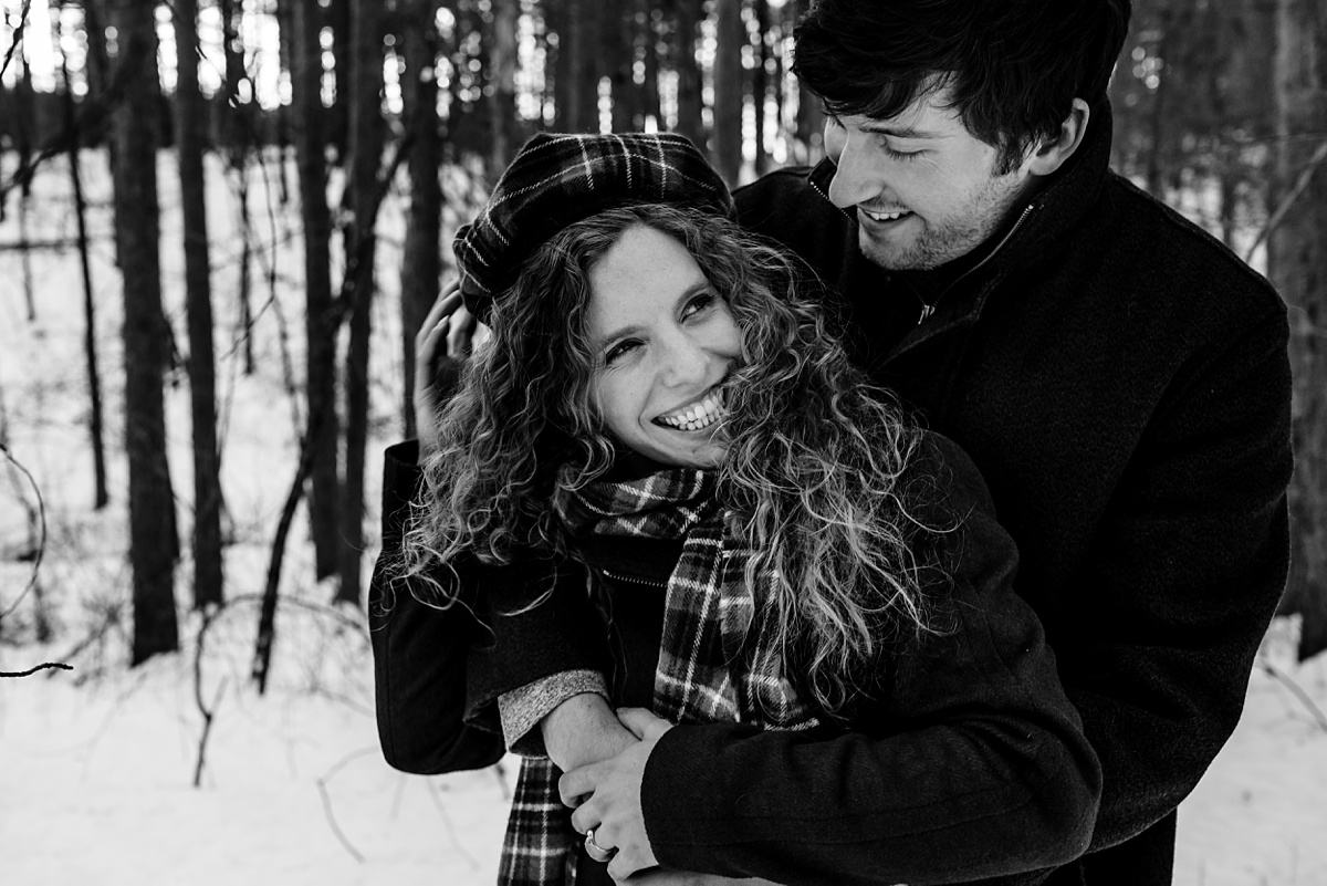 Engagement Session in winter with the happy couple hugging each other tight deep in the snow and woods at Fells Reservation with their Maine Wedding Photographer