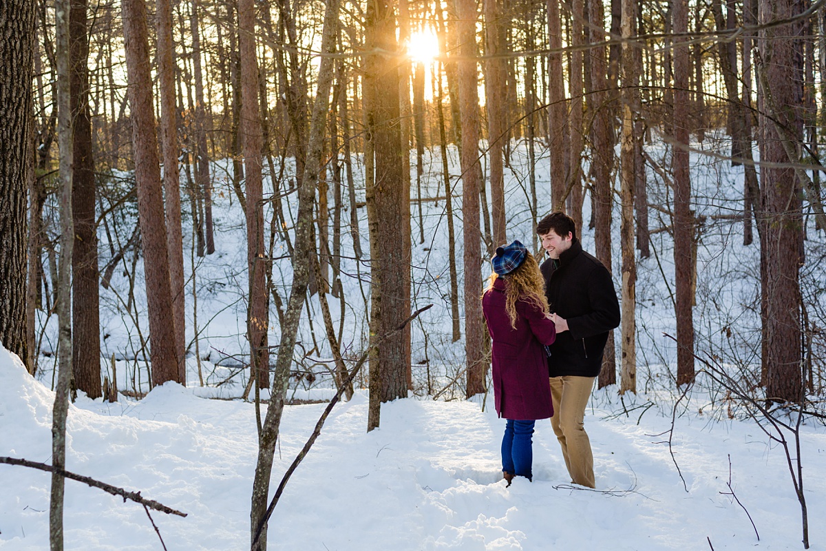 Sun peeking through the snow covered woods of Fells Reservation for the couple's engagement session in winter MA