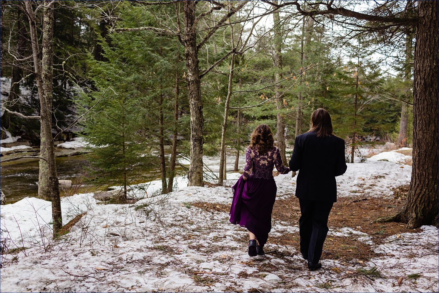 The bride wears her hiking boots with her purple wedding gown out in the spring time woods in Jackson, NH for their elopement adventure