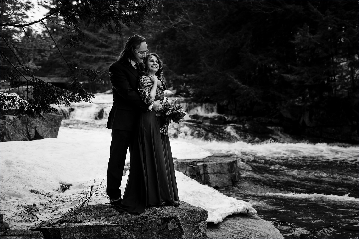 The newlyweds hold on tight to one another in front of Jackson Falls in the Spring chill air after their NH Elopement