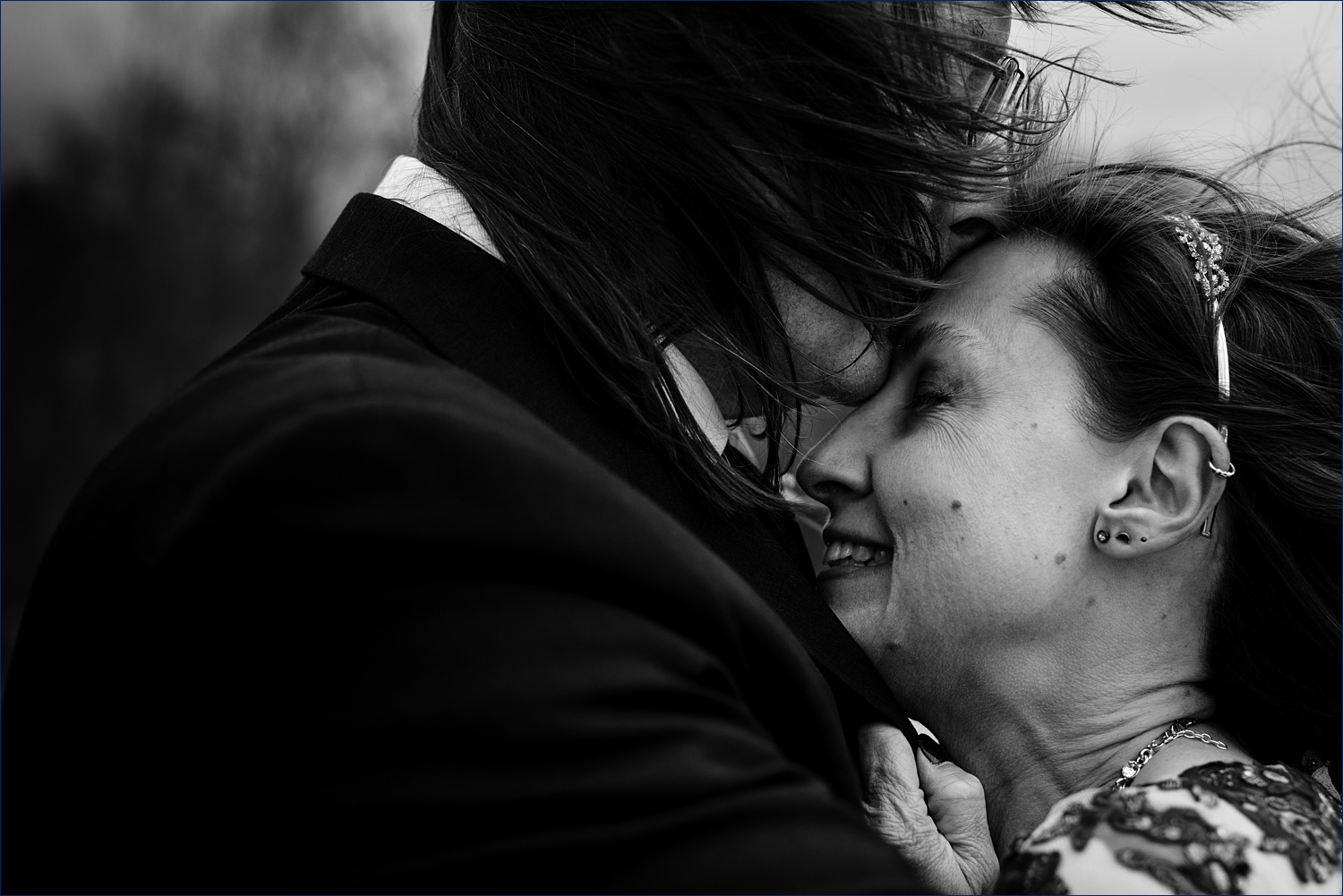 The groom kisses the bride's forehead as she holds tight to him in the wind of the White Mountains after they eloped