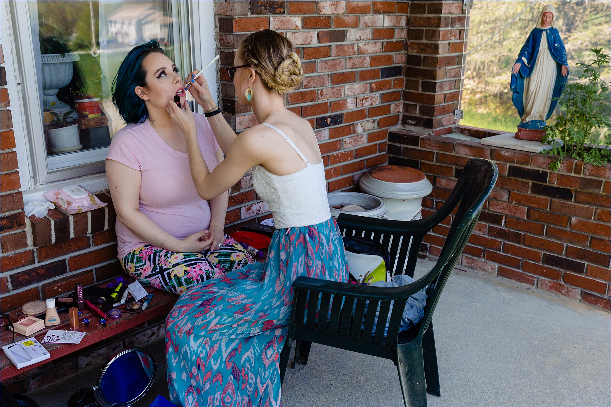 The bride gets her makeup completed on the front porch of the Maine farmhouse while the Virgin Mary watches