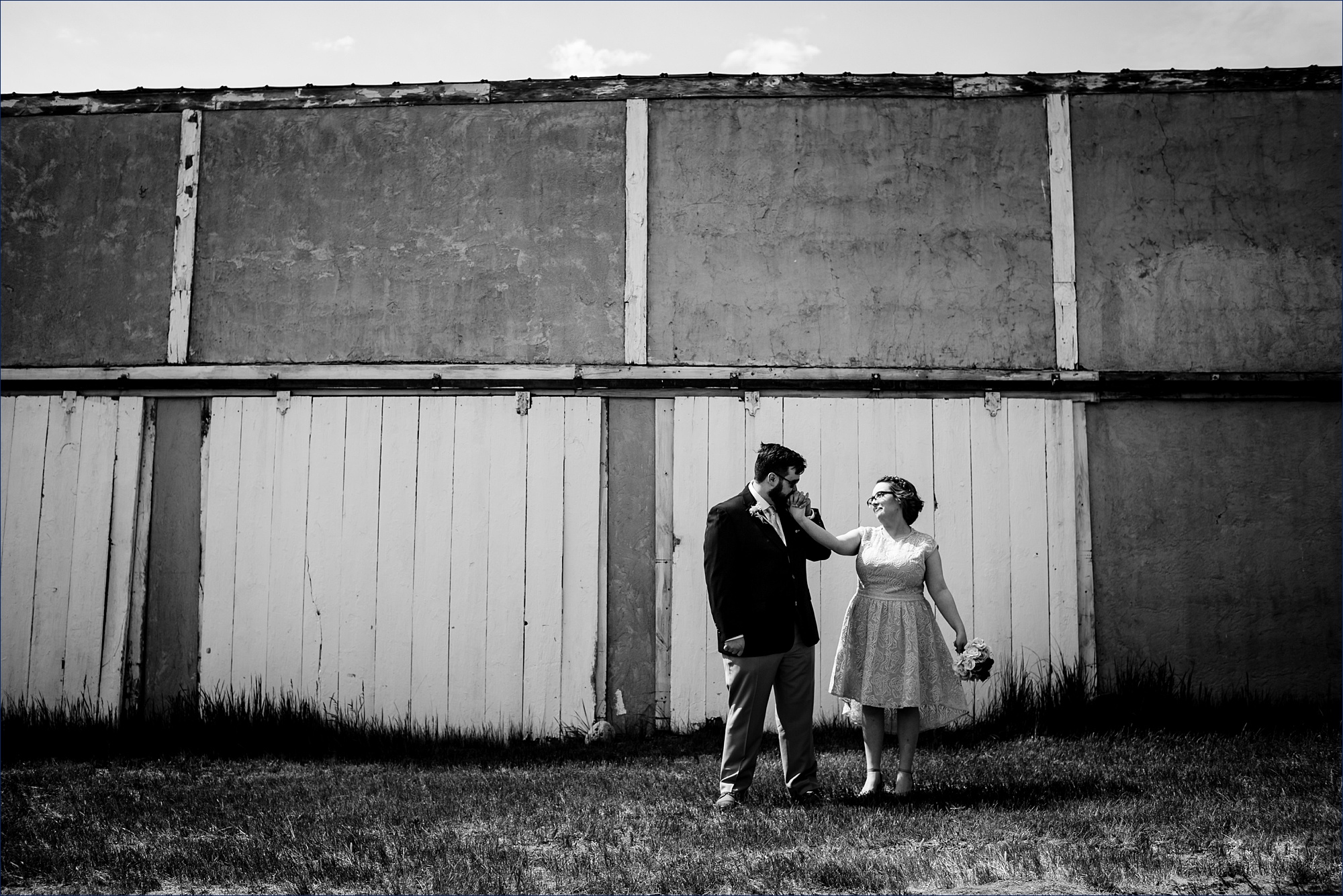 The groom showers the bride with a kiss on the hand in front of a garage at his family's Maine farmhouse