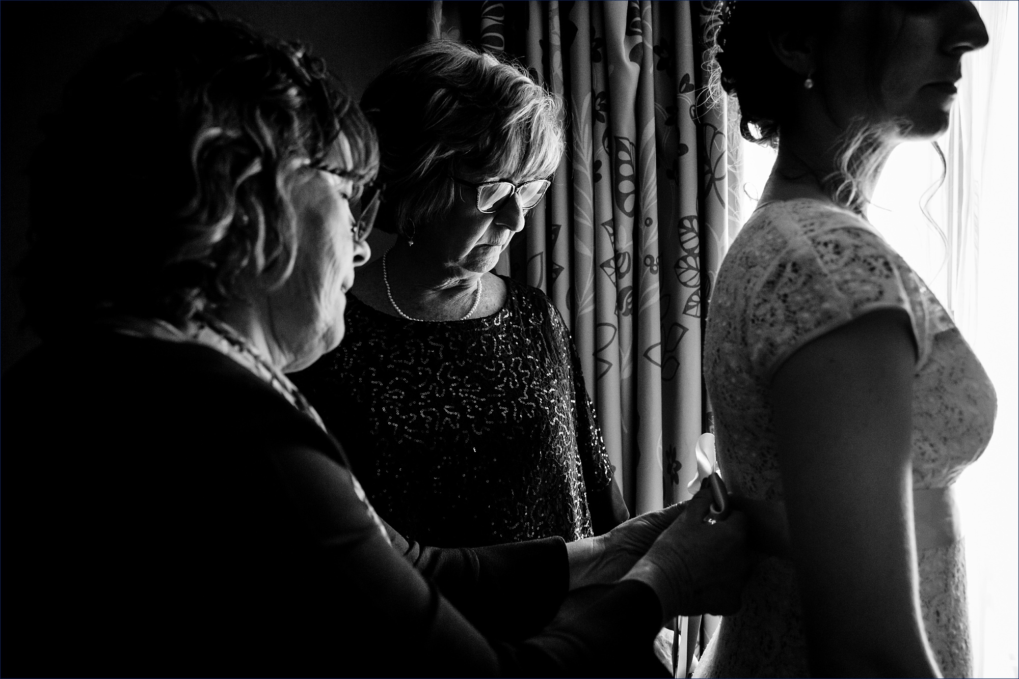 The mother of the bride ties the bow on the bride's wedding dress as they get ready for her wedding day
