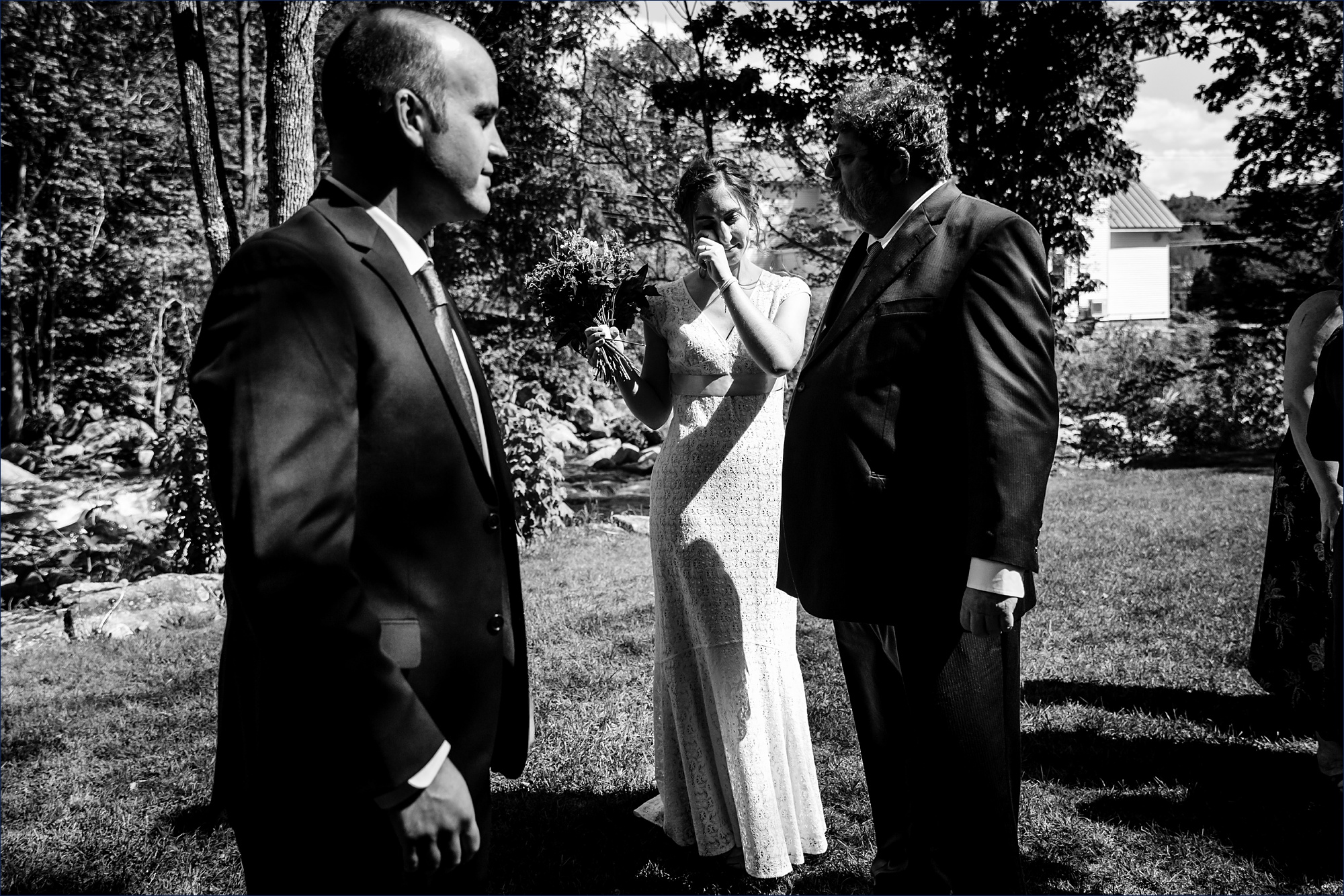 The bride wipes a tear as her new husband and her father stand close after her NH wedding ceremony