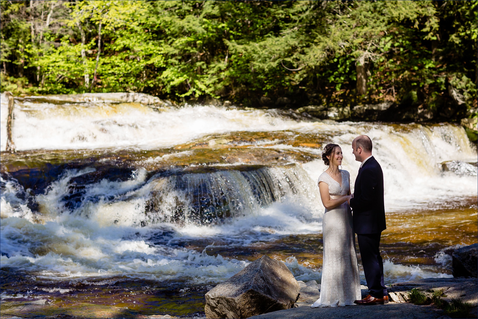 The newlyweds laugh as they stand on the rocks of Jackson Falls New Hampshire after eloping