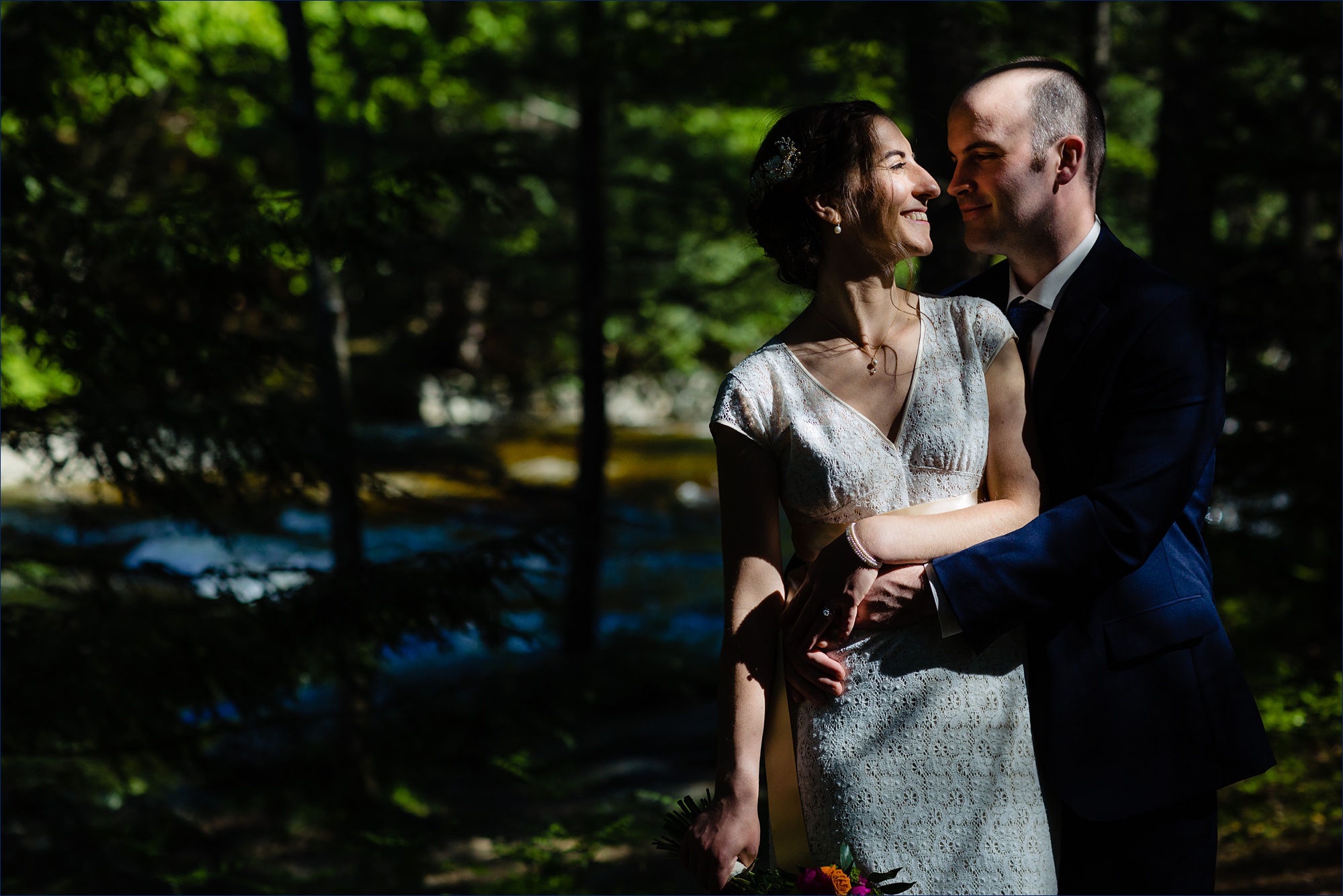 The bright pockets of sun illuminate the couple as they take photos in the woods of New Hampshire after their intimate wedding